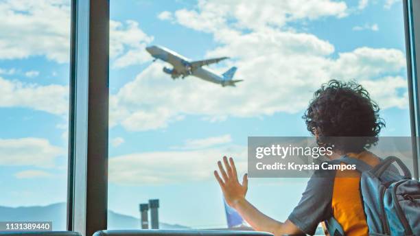 boy watches a plane take off by the airport window - child waiting stock pictures, royalty-free photos & images