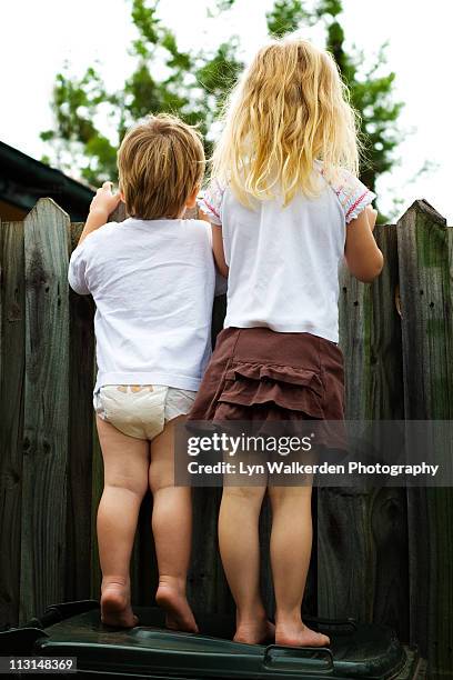 two children looking over a fence - mirar por encima fotografías e imágenes de stock