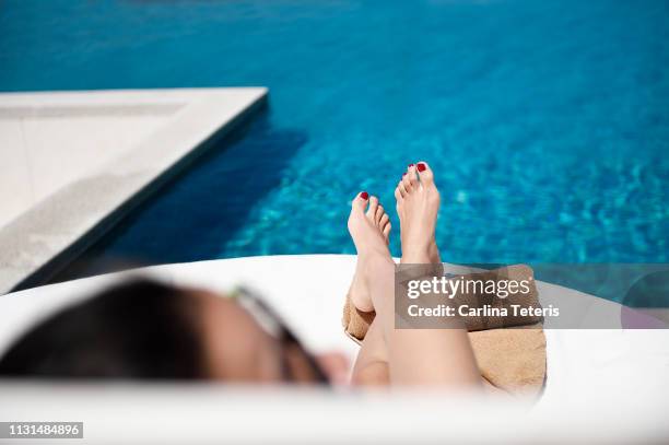 woman's legs on a recliner at a resort swimming pool - fusspflege stock-fotos und bilder