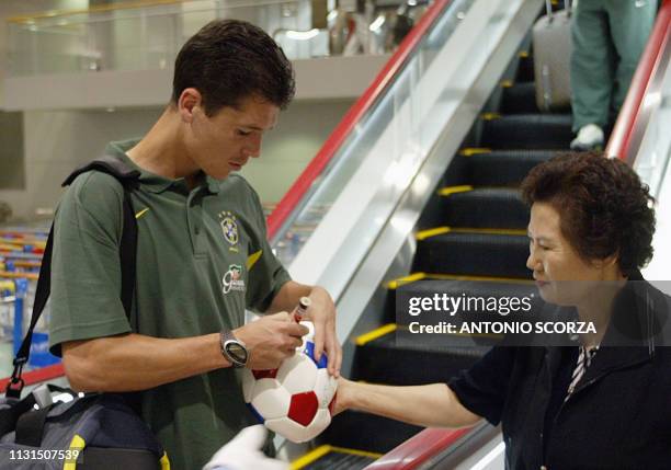 Brazilian soccer player Anderson Polga signs an autograph on a soccer ball to a Japanese soccer fan, 14 June 2002, after his arrival at Kobe airport...