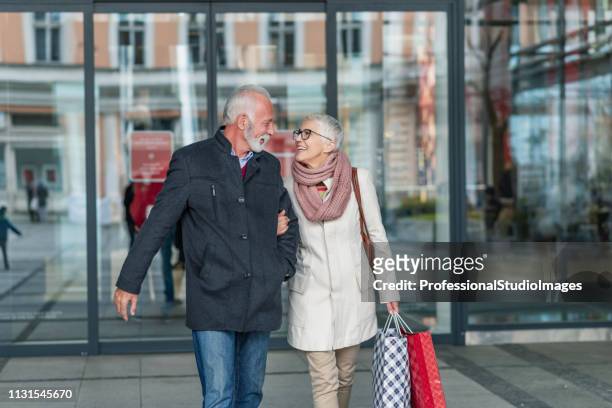 senior couple leaving shopping mall with smile on their faces - leaving store stock pictures, royalty-free photos & images