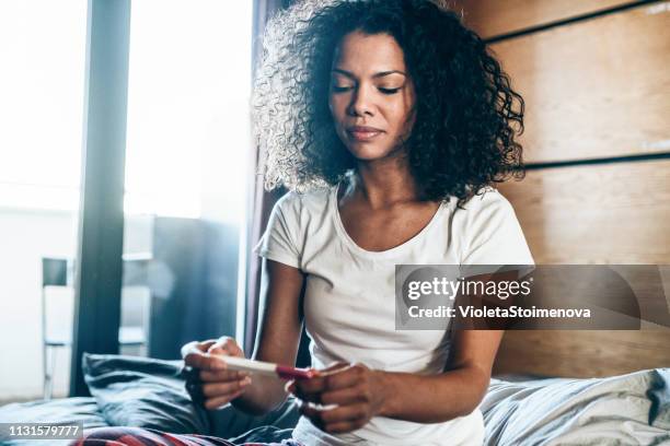 sad young woman with pregnancy test at home - pregnancy test stock pictures, royalty-free photos & images