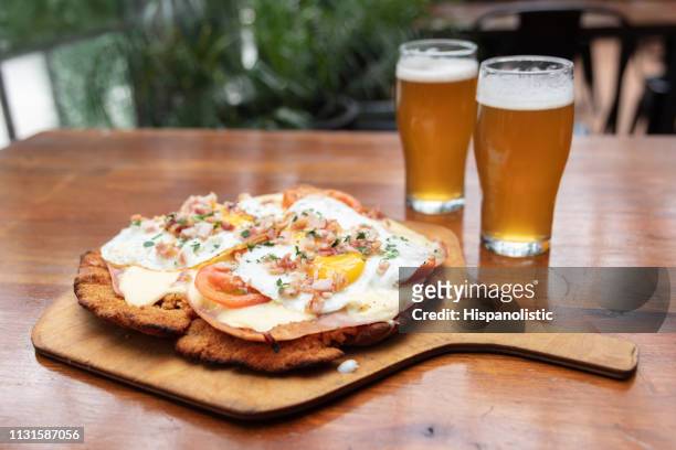 breaded meat with cheese, egg and tomato on top and two beers - schnitzel stock pictures, royalty-free photos & images