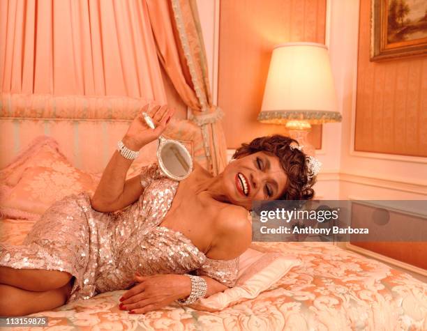 Portrait of actress and singer Eartha Kitt , smiling and holding a mirror, while reclining on a bed, New York, 1992.