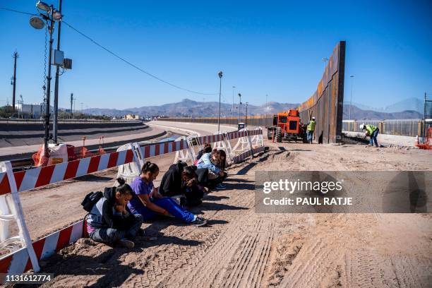 Salvadoran migrants wait for a transport to arrive after turning themselves into US Border Patrol by border fence under construction in El Paso,...