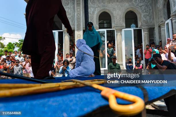 People watch as an Indonesian woman is whipped by a member of the Sharia police in public in Banda Aceh on March 20, 2019. - A group of unmarried...