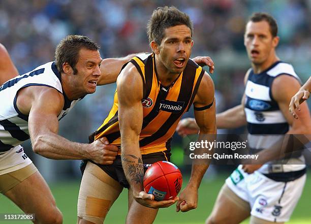 Chance Bateman of the Hawks handballs whilst being tackled by Joel Corey of the Cats during the round five AFL match between the Hawthorn Hawks and...