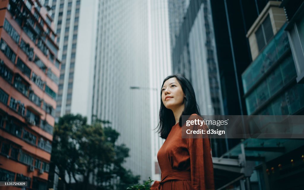 Low angle portrait of confidence young woman standing against highrise city buildings in city