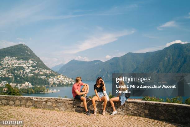 friends relax on lake promenade below mountains - promenade seafront stock pictures, royalty-free photos & images