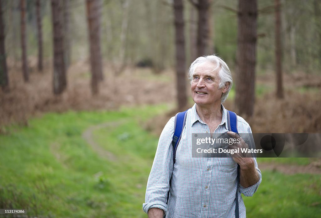 Senior man walking along forest path.