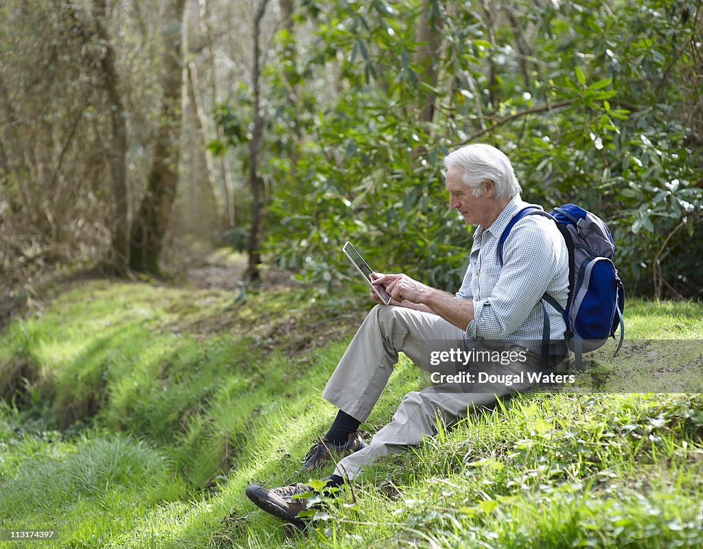 Senior man sitting on grass using digital tablet.