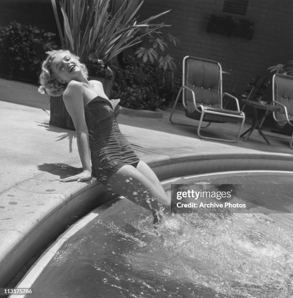 American actress Marilyn Monroe wearing a bathing suit and with her legs in a swimming pool circa 1951.