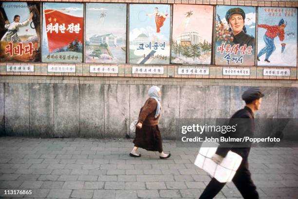 Man and a woman walking past a selection of posters, North Korea, February 1973.