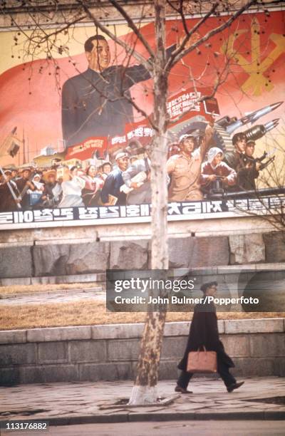 Man walking past a poster depicting Communist leader Kim Il-sung and North Korean revolutionary forces, North Korea, February 1973.