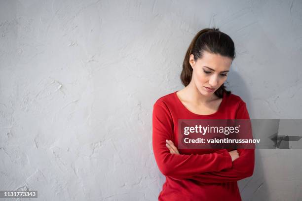 mujer infeliz mujer de pie con los brazos cruzados sobre fondo gris - culpabilidad fotografías e imágenes de stock