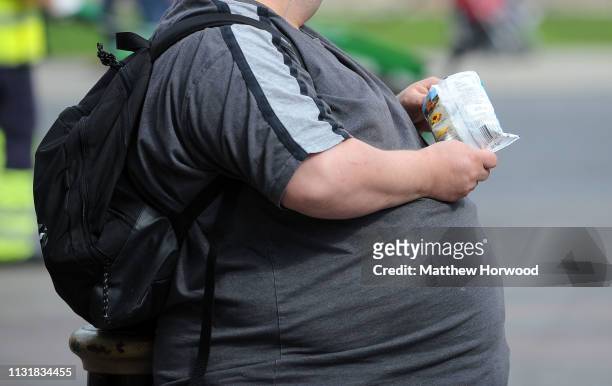 An overweight man with an obscured face eats crisps on March 29, 2009 in Cardiff, United Kingdom.