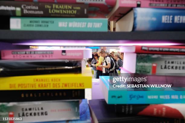 Visitors are seen behind a pile of books on display at the booth of the Random House publishing house at the Leipziger Buchmesse book fair in...