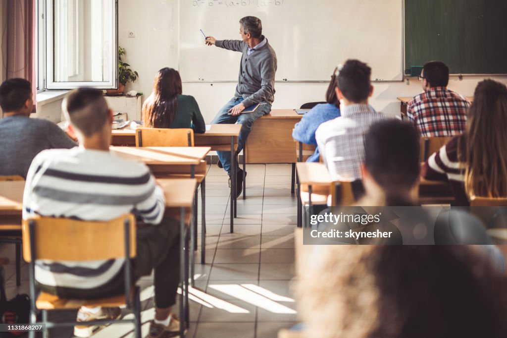 Mitteler erwachsener Lehrer, der seinen Schülern im Klassenzimmer einen Vortrag hält.