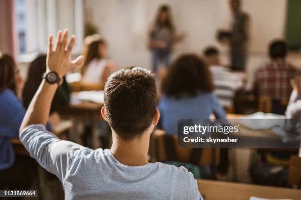 back view of male student raising hand on a class. - raised hand stock pictures, royalty-free photos & images