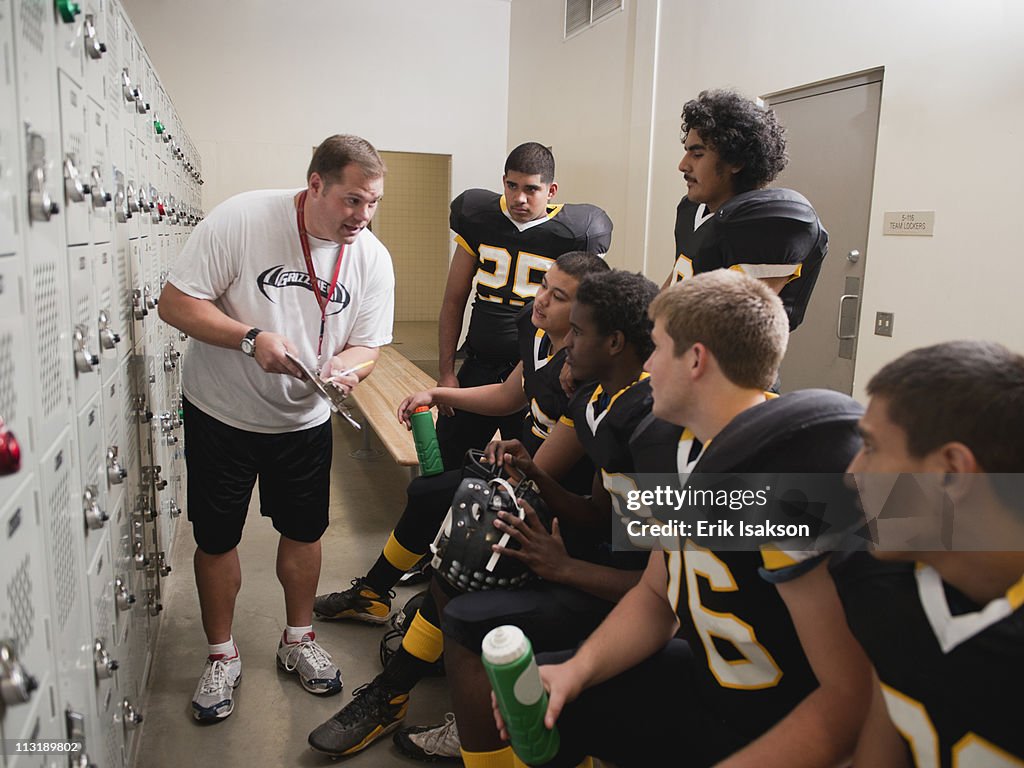 Coach talking to football players in locker room