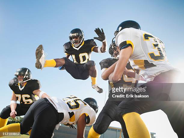 football player leaping over players on football field - tackle american football positie stockfoto's en -beelden