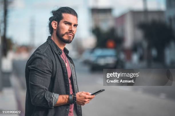 thoughtful mid adult man with smart phone in city - man bun stock pictures, royalty-free photos & images