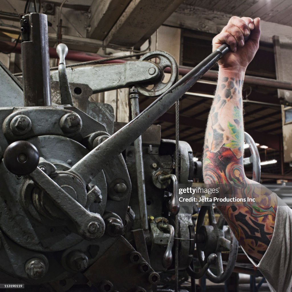 Caucasian worker with tattoos pulling lever in factory