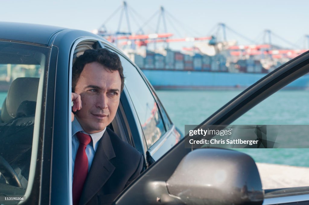 Hispanic businessman using cell phone in car with container ship in background