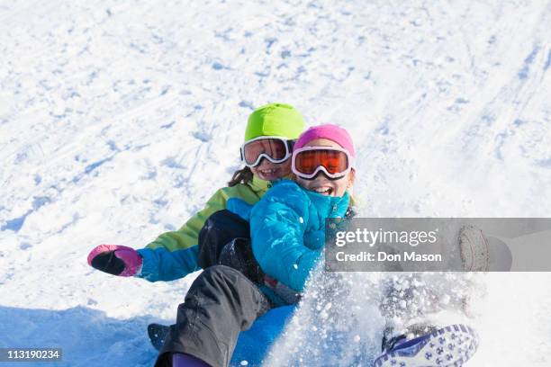 mixed race girls sledding in snow - asian family fall stock-fotos und bilder