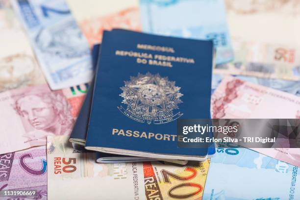 brazilian passport on top of brazilian real notes of various values - finanças stock-fotos und bilder