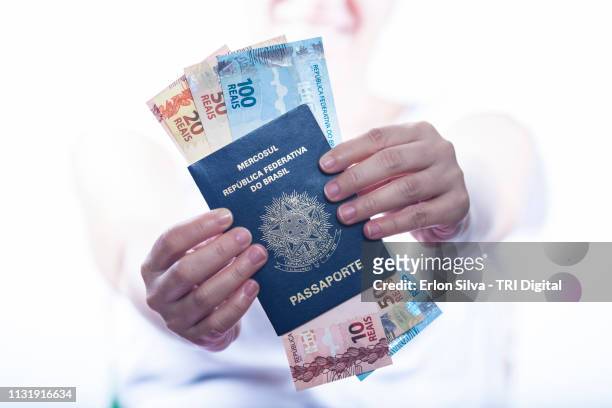 woman holding and showing the brazilian passport with a lot of brazilian real money inside - mão no cabelo stockfoto's en -beelden