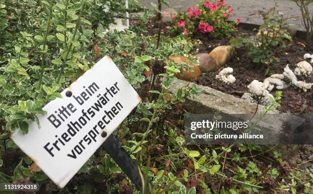August 2017, North Rhine-Westphalia, Löhne: A sign with the inscription "Bitte beim Friedhofswärter vorsprechen" can be seen on a grave of a...