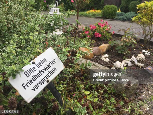 August 2017, North Rhine-Westphalia, Löhne: A sign with the inscription "Bitte beim Friedhofswärter vorsprechen" can be seen on a grave of a...