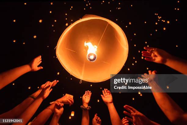 group of hands together releasing the flying lantern with numerous lanterns in the sky, yeepeng festival , chiangmai, thailand - windlicht stock-fotos und bilder