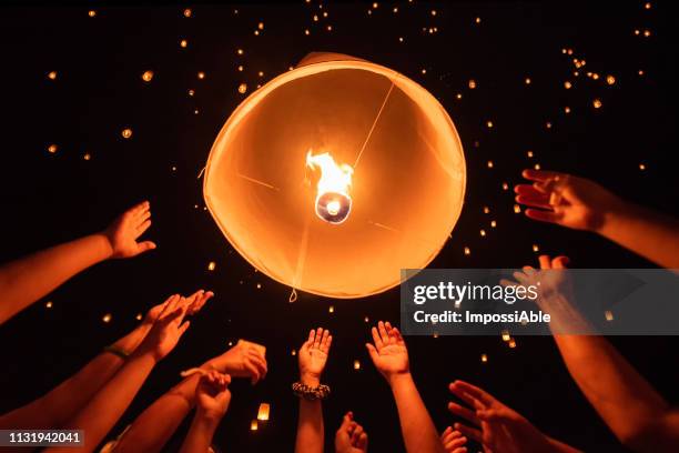 group of hands together releasing the flying lantern with numerous lanterns in the sky, yeepeng festival , chiangmai, thailand - jack o lantern fotografías e imágenes de stock