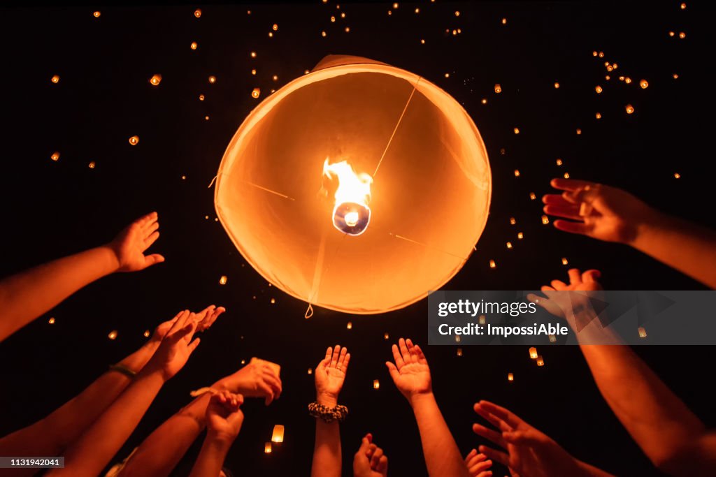 Group of hands together releasing the flying lantern with numerous lanterns in the sky, yeepeng festival , Chiangmai, Thailand