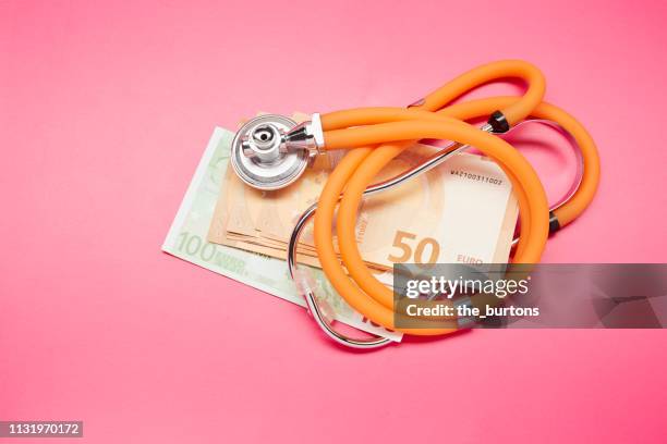 high angle view of stethoscope and euro banknotes on colored background - zorgverzekering stockfoto's en -beelden