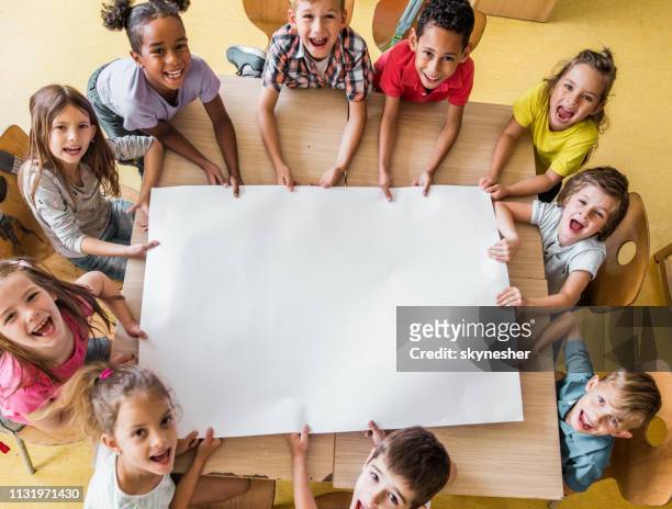 über der ansicht glücklicher grundschüler mit leerem papier im klassenzimmer. - holding aloft stock-fotos und bilder