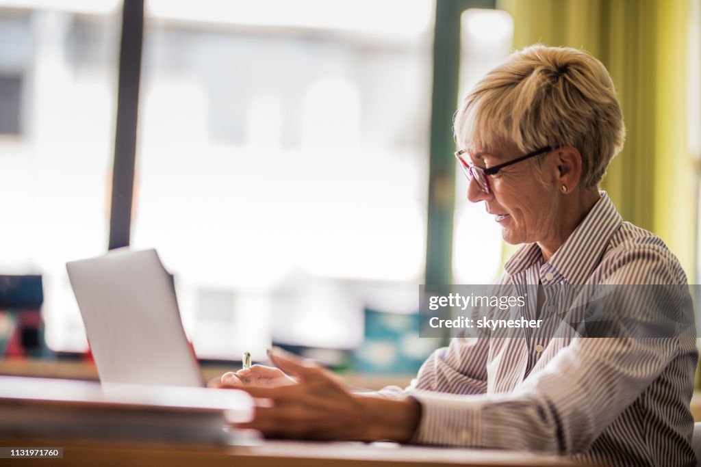 Smiling senior teacher taking notes in the classroom.