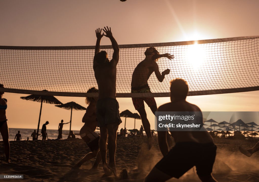 Jeunes amis s'amuser tout en jouant au Beach-volley au coucher du soleil.