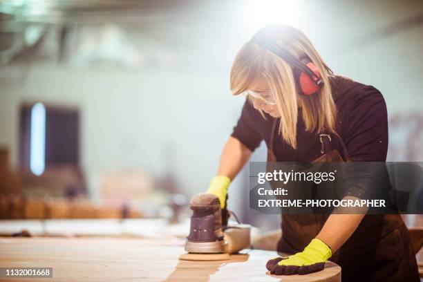 girl carpenter using an orbit sander to sand down a wooden panel on a work bench in a workshop - sand paper stock pictures, royalty-free photos & images