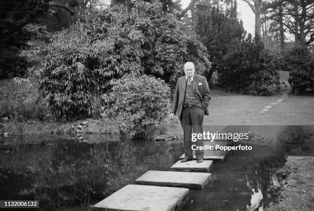 British politician Winston Churchill pictured standing on stepping stones over a pond in the grounds of Chartwell country house near Westerham in...