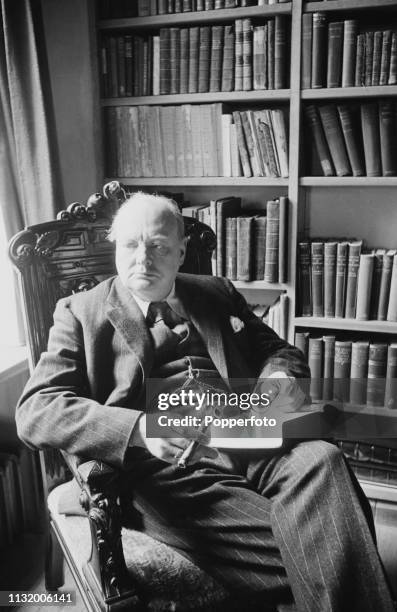 British politician Winston Churchill pictured seated with a book and cigar in the library of Chartwell country house near Westerham in Kent, England...