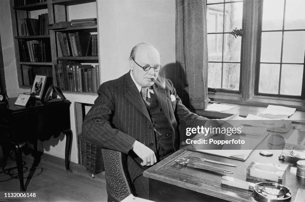 British politician Winston Churchill pictured seated with a cigar at a desk in the library of Chartwell country house near Westerham in Kent, England...