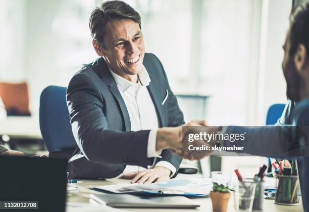 happy mid adult insurance agent shaking hands with his customer in the office. - investment manager stock pictures, royalty-free photos & images