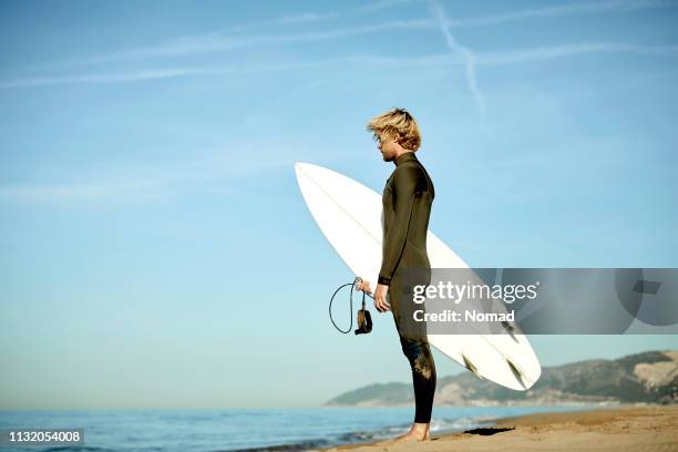 homme avec la planche de surf restant sur le rivage à la plage - planche de surf photos et images de collection