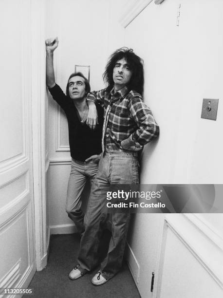 Bernie Taupin, British songwriter, standing beside U.S. Rock singer Alice Cooper, circa 1975. Copper leans against a wall with his arm on Taupin's...
