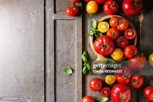 Variety of ripe fresh organic gardening tomatoes different kind and colors with water spot and basil leaves on wood cutting board over old grey...