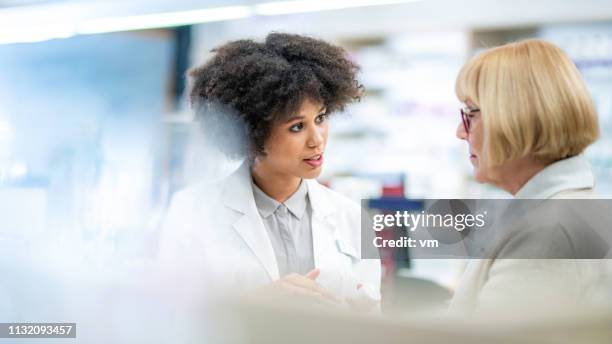 mujer mayor hablando con una farmacéutica femenina - pharmacist fotografías e imágenes de stock