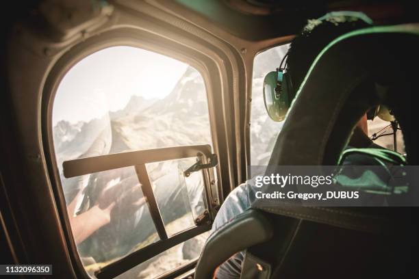 helicopter cockpit with rear view of unrecognizable men co-pilot flying over mont blanc massif in french alps mountains at sunset - helicopter window stock pictures, royalty-free photos & images